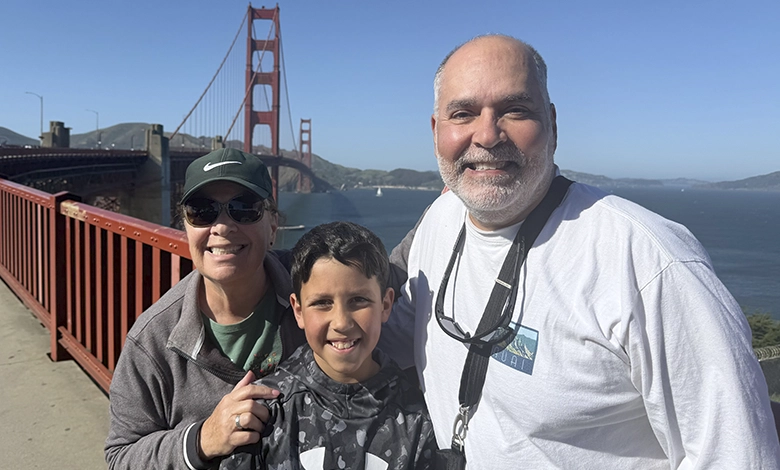Grandmother, grandson and grandfather smiling on the Golden Gate Bridge walkway with the bridge and bay behind them