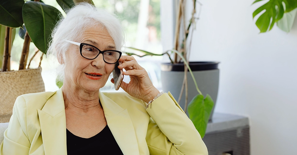 Older woman with glasses talking on her mobile phone at home