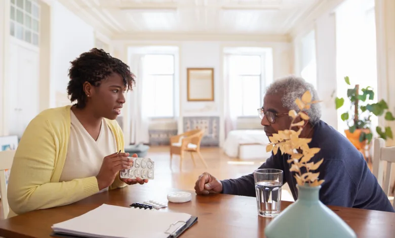 Caregiver and older man reviewing his medications together at a dining table