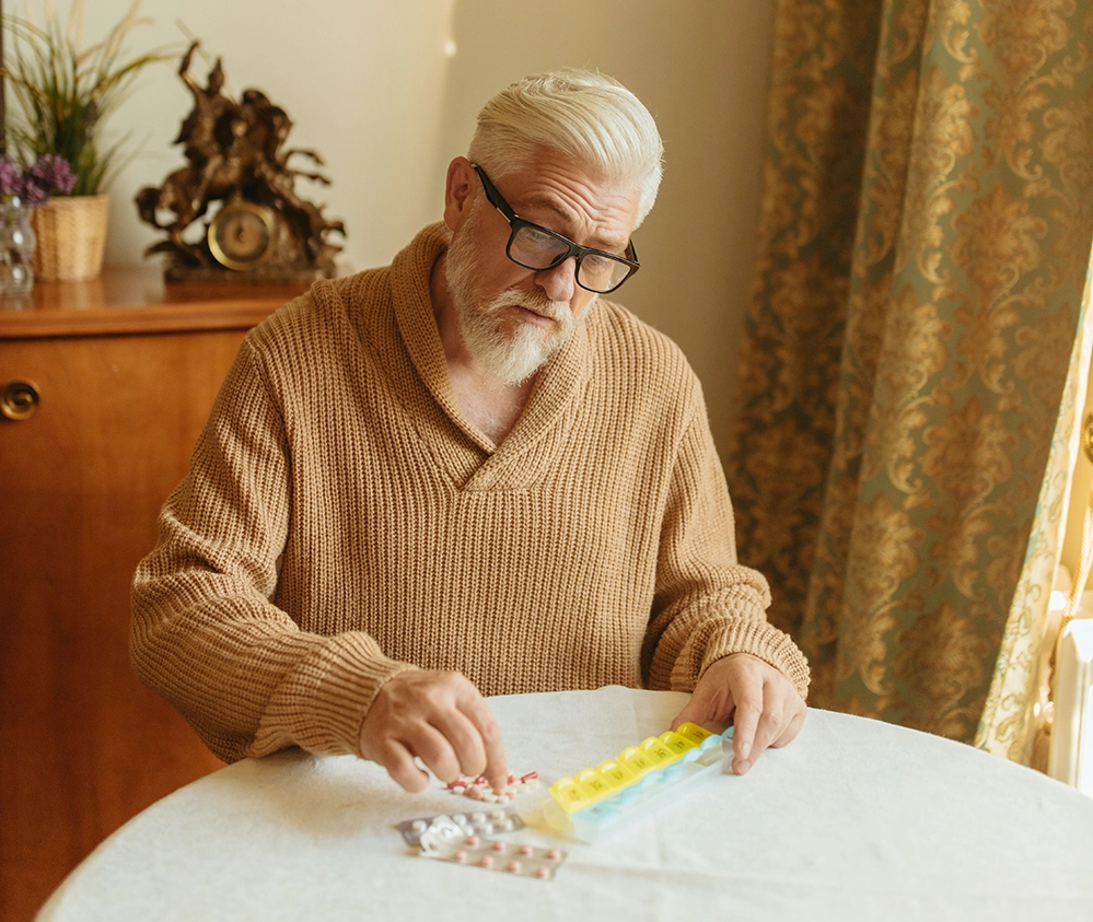 Managing Chronic Conditions After 65: Systems That Hold 2 Older man filling a weekly pill organizer at his dining table