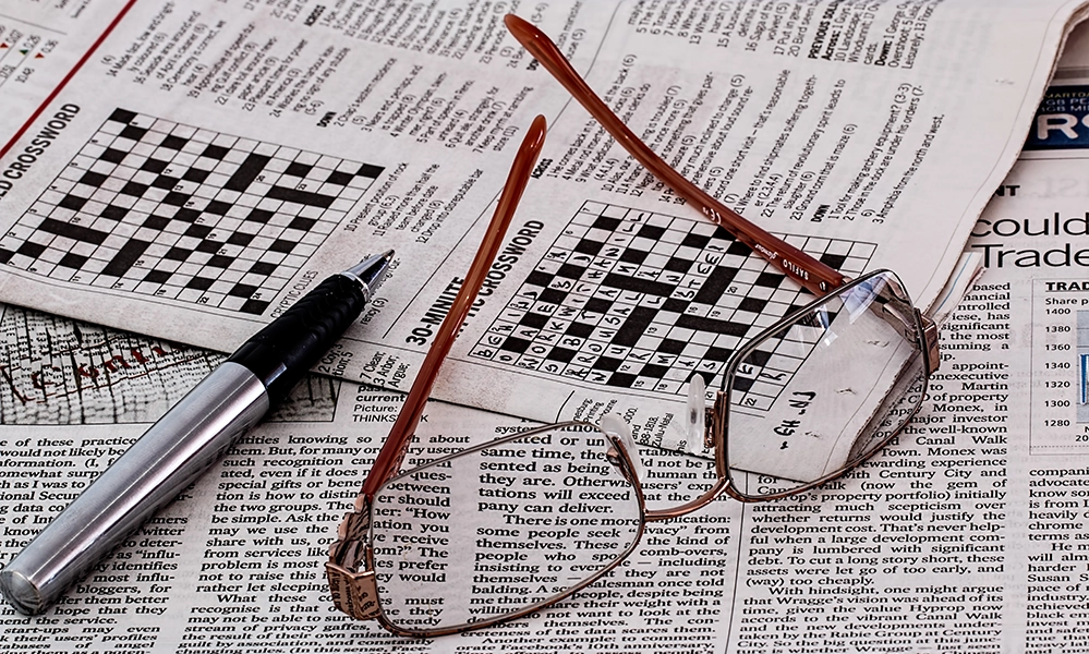 A half-finished newspaper crossword with a pen and reading glasses set on top