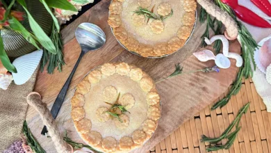 Two crab and corn pot pies with scalloped pastry edges and fresh tarragon on a wooden board