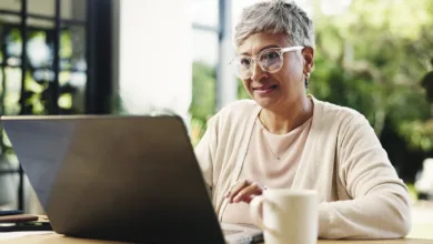 An older woman reading at her laptop in a sunlit room