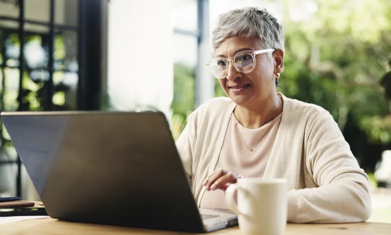 An older woman reading at her laptop in a sunlit room