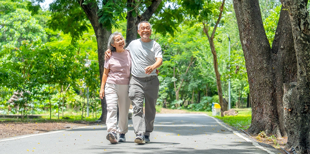 An older couple walking briskly together on a tree-lined park path
